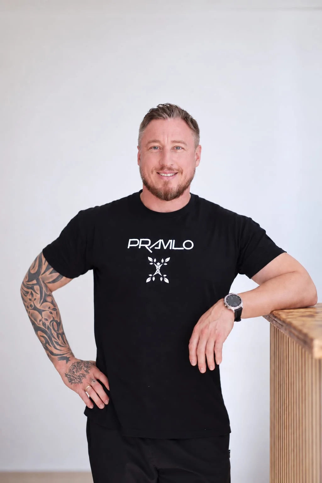 Andreas Klaus im schwarzen Pravilo-Shirt, an einen Holztresen in der Praxis gelehnt