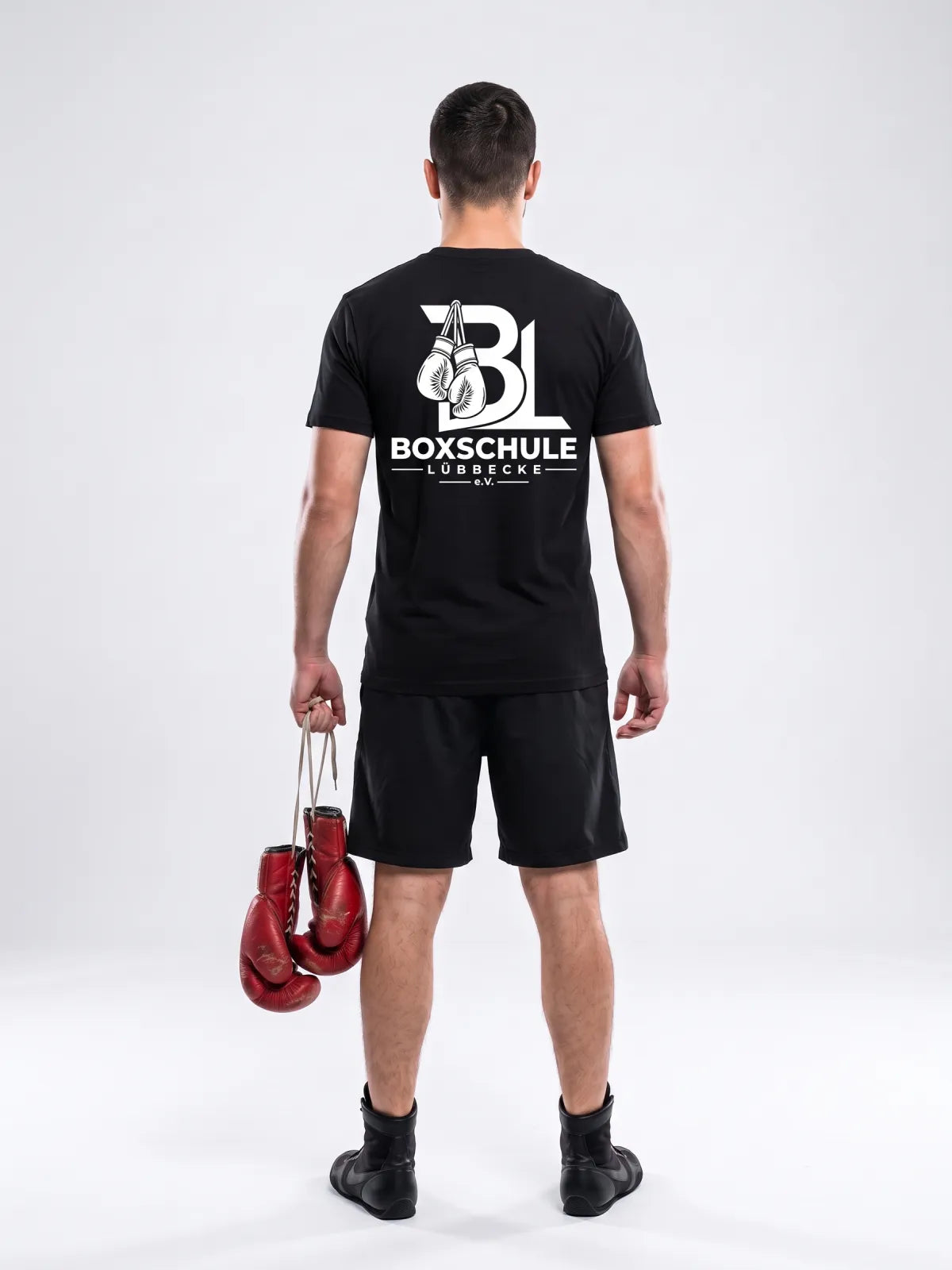 Boxer von hinten im schwarzen Vereinsshirt mit dem Wappen der Boxschule Lübbecke, rote Boxhandschuhe in der Hand